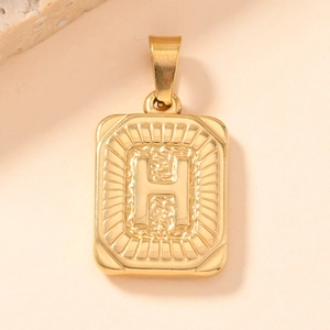 Macro detail of a vintage gold-plated square pendant with embossed letter H and textured finish