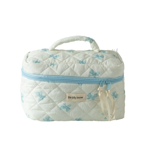Quilted makeup bag with blue bow prints and double zipper on a white background