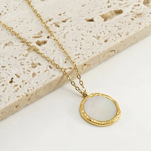 Detail view of a round white shell pendant with a golden hammered texture edge on a chain
