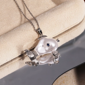 Macro detail of silver fish necklace with baroque pearl and blue gemstone eye on mirror
