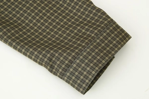 Detailed close-up of brown and green plaid shirt cuff showing fine stitching and fabric