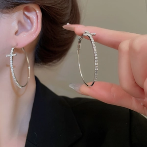 Gros plan de boucles d'oreilles créoles argentées avec breloques croix et strass