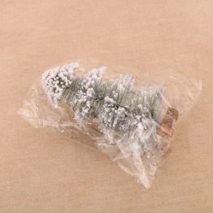 Close-up of artificial snow-flocked pine tree with a wooden base in clear packaging
