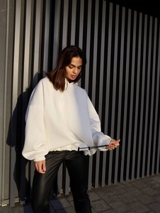 Oversize white hoodie with back embroidery on a model against a gray geometric wall