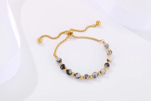 Detail of adjustable gold bead bracelet with dalmatian stone charms on white silk