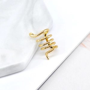 Macro detail of golden snake-shaped ear cuff with textured scales on marble background