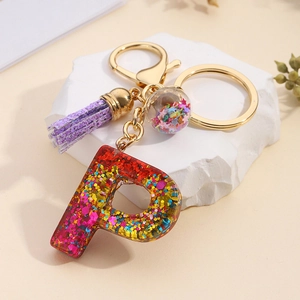 Detail of resin letter P keychain with purple tassel and colorful star sequins in gold hardware