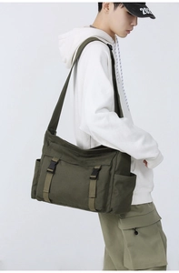 Vue latérale du sac messager en toile vert olive avec boucle en plastique noir et poche latérale