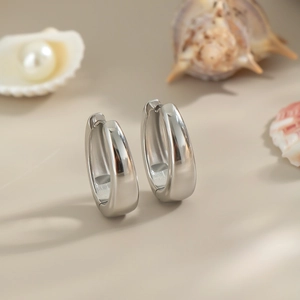 Detailed view of polished silver U-shape hoop earrings on beige surface with pearls