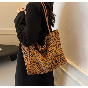 Side view of a large leopard print tote bag on shoulder with brown straps on black coat