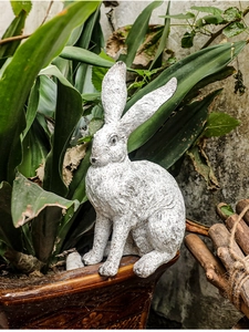 Close-up of a weathered resin bunny garden statue perched on a rustic flower pot