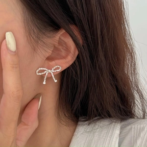 Close-up of s925 silver bow stud earrings worn on ear showing delicate metal texture