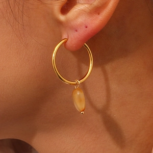 Detailed close-up of a gold hoop earring with a translucent amber stone pendant on ear