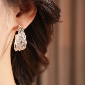 Close-up of model wearing silver woven texture C-shape earrings with a metallic finish