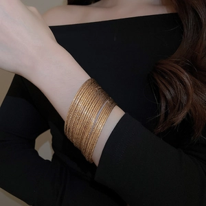 Close-up of a stacked set of 20 polished gold-tone metallic bangles on a model's wrist
