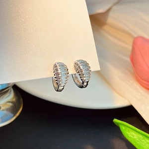 Détail de boucles d'oreilles créoles argentées avec motif texturé à nervures horizontales