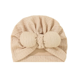 Detail of baby knit turban hat featuring large bow and textured jacquard in beige