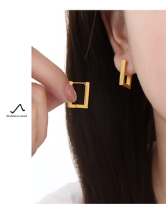 Close-up of golden rectangular stainless steel hoop earring worn on a female model