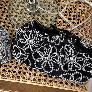 Top view of black fabric clutch featuring elegant white floral embroidery on woven rattan