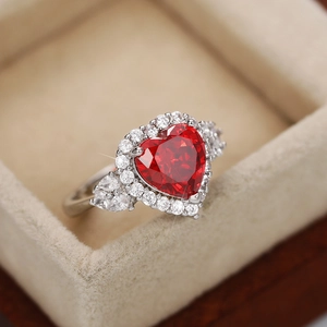 Macro shot of silver ring with heart-shaped red gemstone in a beige velvet jewelry box