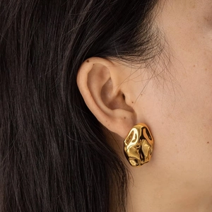 Close-up of golden irregular lava texture earrings with minimalist mirror finish
