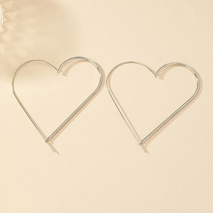 Macro shot of large silver heart-shaped hoop earrings on a textured beige surface