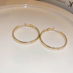 Close-up of gold-plated hoop earrings on a white ceramic tray with polished finish