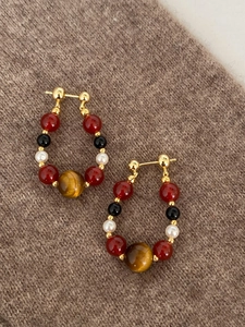 Detailed close-up of tiger eye and pearl beaded earrings on a warm brown knit texture