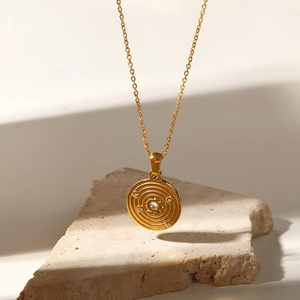 Macro detail of a gold medallion pendant with starburst engraving and a tiny zircon stone