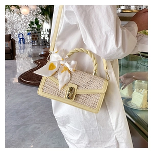 Close-up of summer straw crossbody bag with twist handle, gold clasp and decorative silk scarf