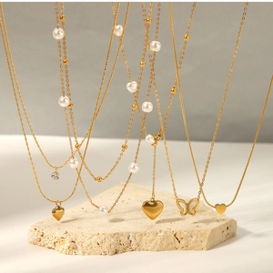 Gros plan de colliers dorés avec pendentifs cœur et papillon sur pierre blanche
