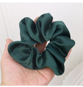 Detail of a dark green satin oversized scrunchie showing its glossy silk-like texture
