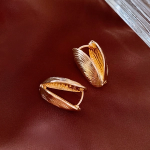 Detailed macro view of gold shell textured metal earrings on a dark silk fabric background
