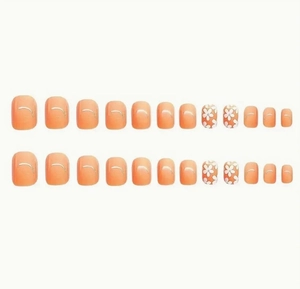 Détail de faux ongles de pieds orange pêche avec motifs floraux blancs et traits dorés