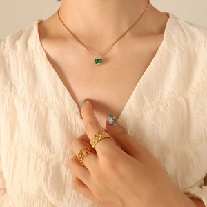Golden necklace with emerald green stone pendant and textured rings on model