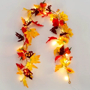 Close-up of lighted autumn garland with maple leaves, mini pumpkins and red berries