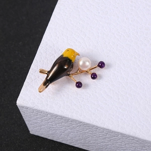 Macro detail of a colorful bird brooch with white pearl on a golden branch