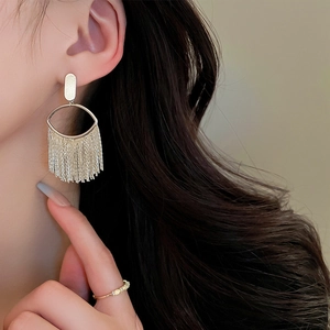 Close-up of gold-plated oval stud earrings with elegant long metal fringe tassels