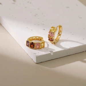 Gold hoop earrings with multicolored rectangular stones on a natural stone display