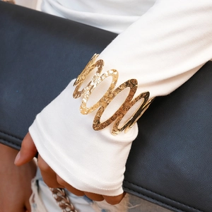 Close-up of golden hammered wavy cuff bracelet worn over white knit sleeve