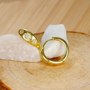 Macro shot of gold sunflower hoop earring with starburst zircon on natural wood base