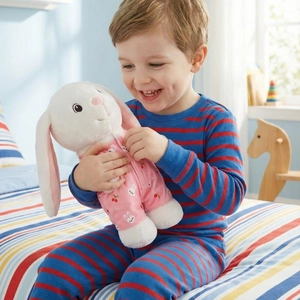 Cute white bunny plush toy in pink cherry pajamas held by a smiling child in a room