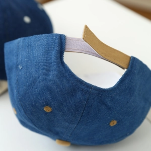 Dettaglio della chiusura regolabile sul berretto di jeans blu scuro per neonati
