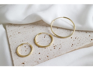Detailed view of three minimalist gold hoop earrings in various sizes on a stone base