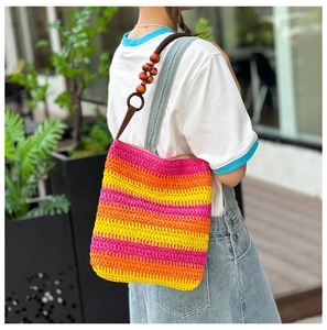 Detail of rainbow straw tote bag featuring wooden beads and brown leather shoulder strap