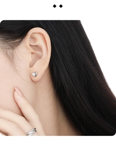 Close-up of minimalist silver heart stud earring with a small diamond on model's ear