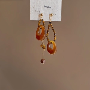 Detailed close-up of asymmetric ethnic earrings with amber beads and shell tassel