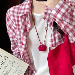 Close-up of a handmade red fabric apple pendant on a woven cord necklace for women