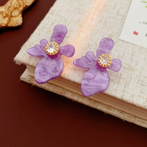 Vue détaillée de boucles d'oreilles fleurs en résine violette avec zircon sur un livre