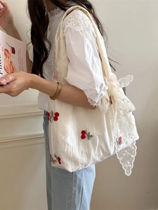 Chic tote bag with cherry embroidery and lace bow accent on a soft textured fabric